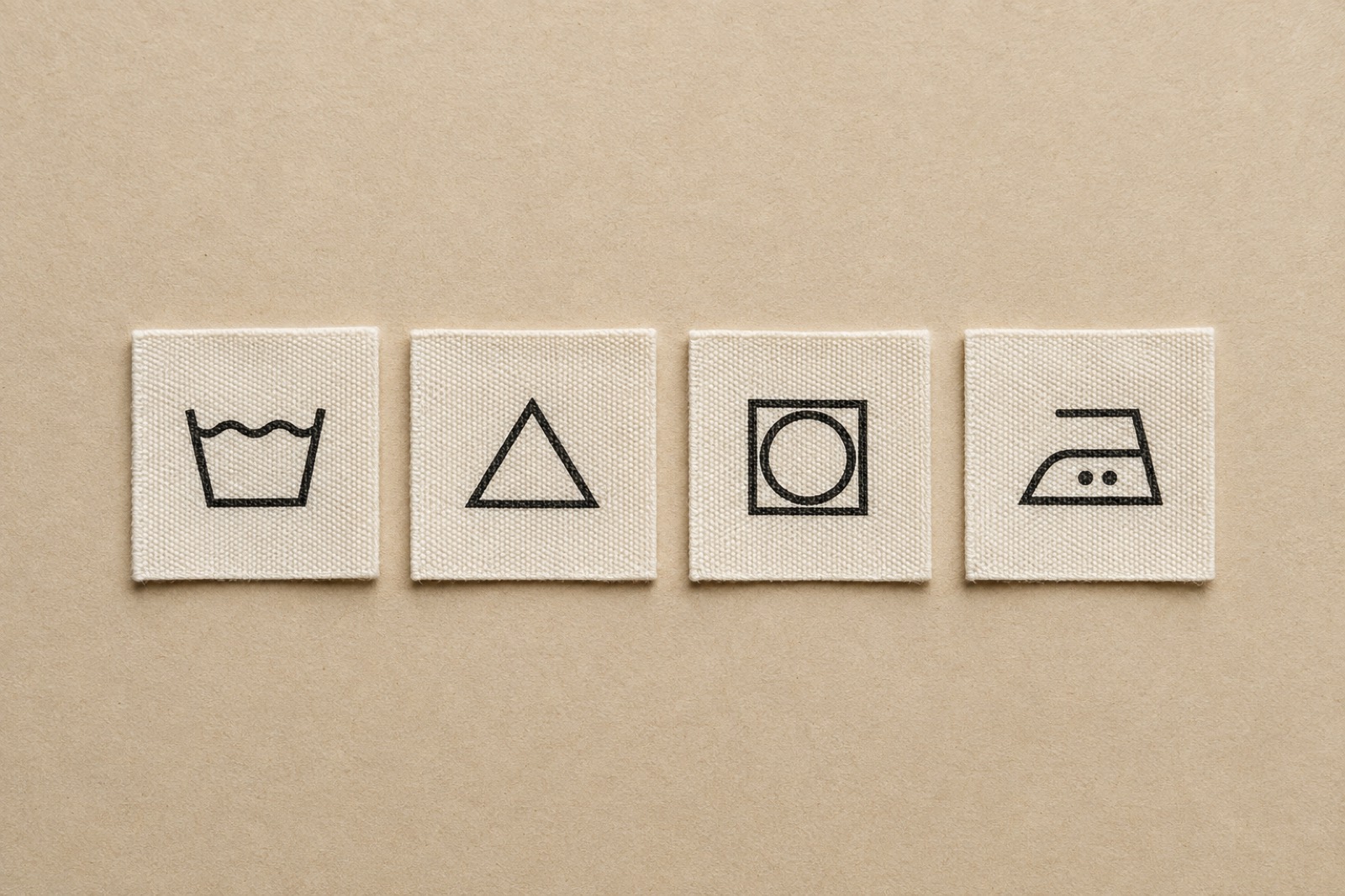 A row of woven care labels laid flat, showing wash tub, triangle, square and iron symbols.